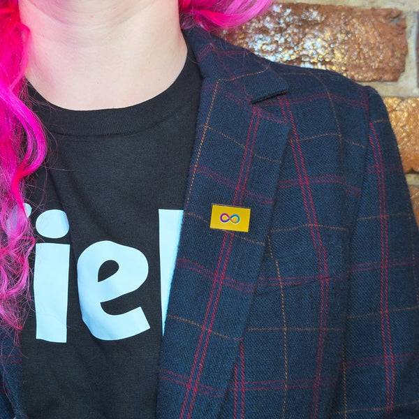An autistic pride pin on the lapel of a woman