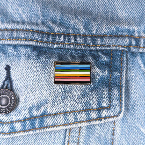 An image of a queer pin on a denim jacket pocket
